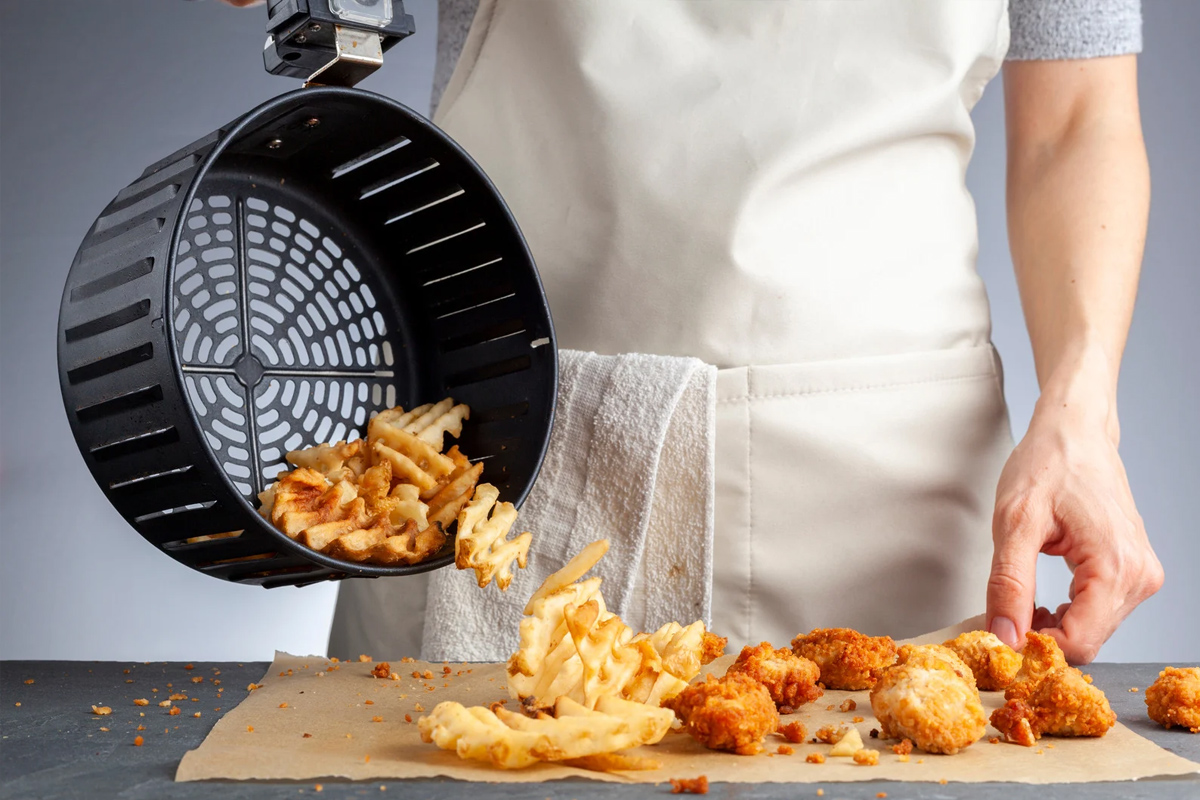 Personne déchargeant des frites de gaufres fraîches d'une friteuse à air