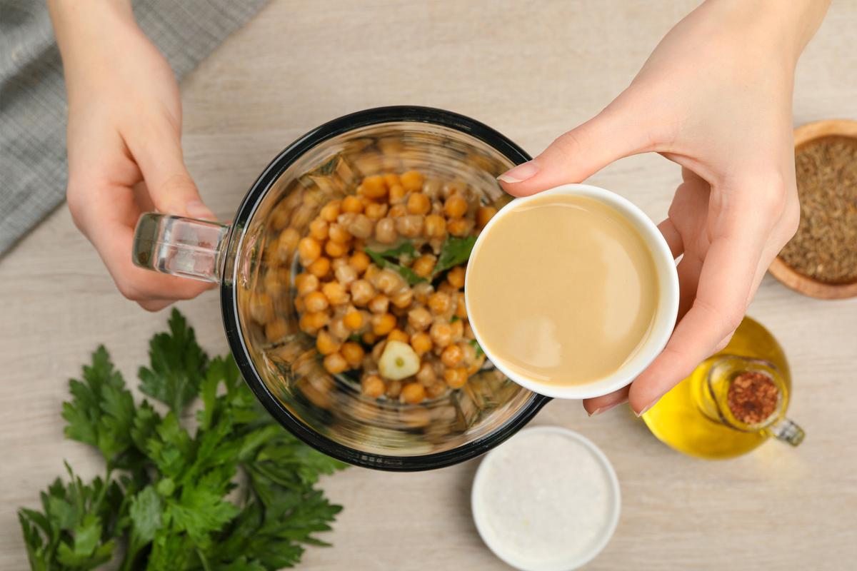 Femme ajoutant de la tahina dans le mixeur avec des ingrédients pour le houmous